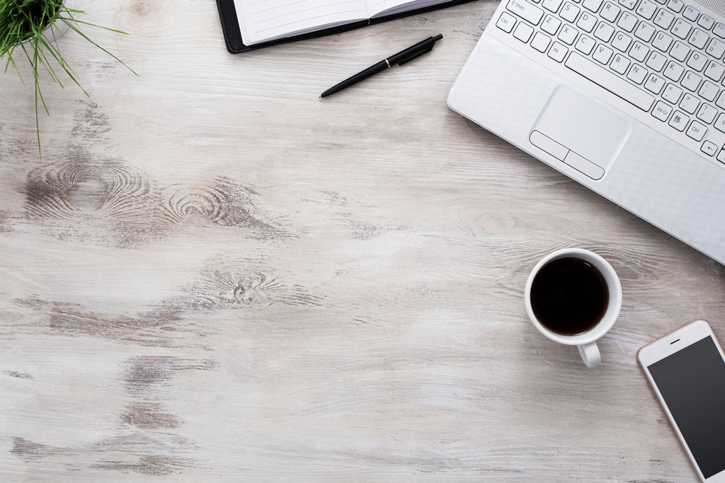 A laptop, a pen and a cup of coffee sit on a desk.
